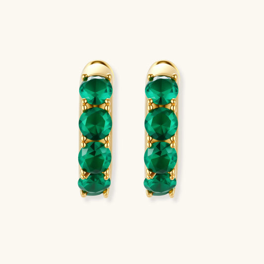 Close-up of gold-plated huggie hoop earrings featuring four emerald green cubic zirconia stones on white background.